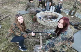 dwie dziewczynki przecinają piłką drewno, w tle siedzą inne dzieci