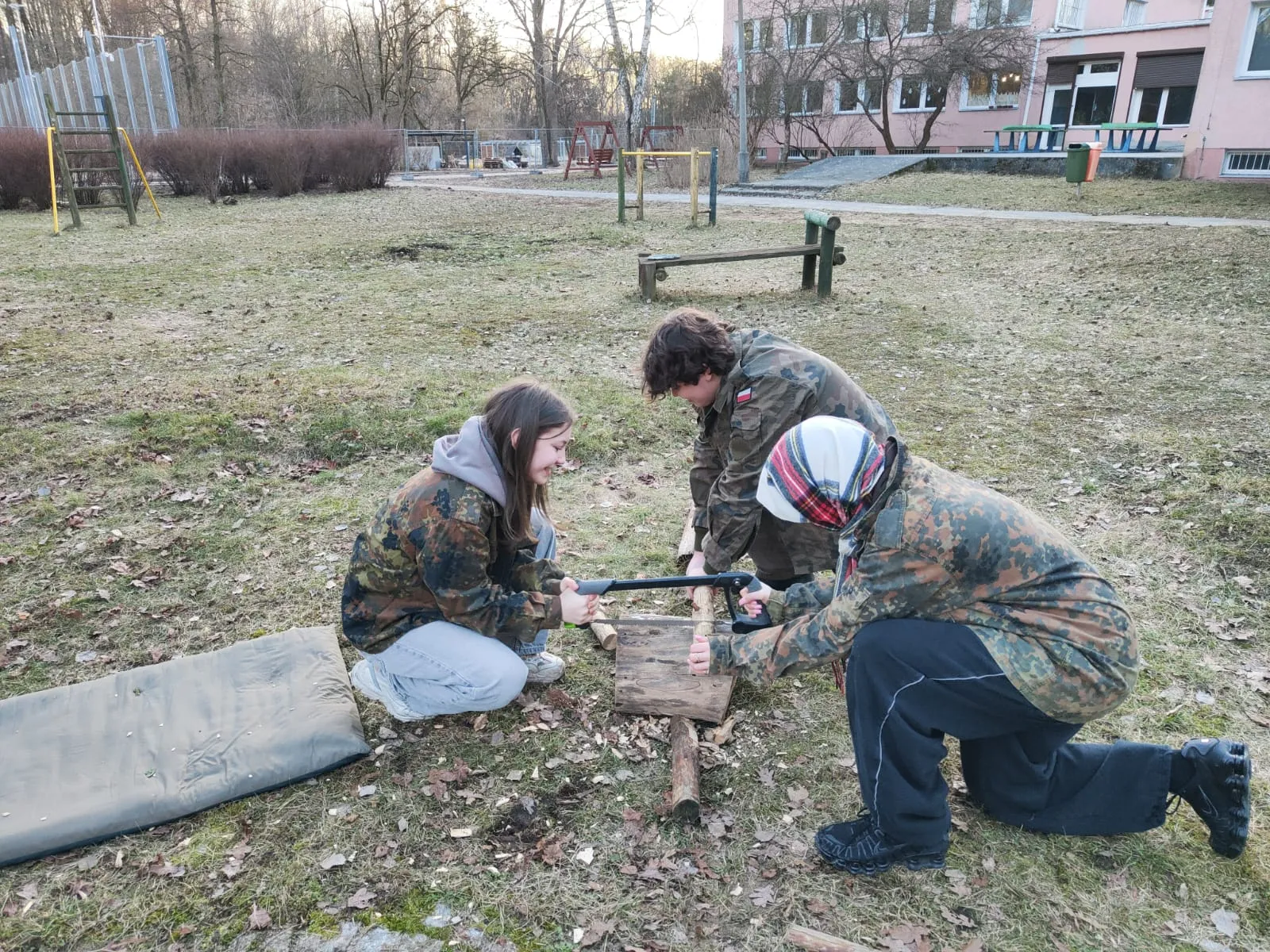 troje uczniów próbuje przeciąć drewno